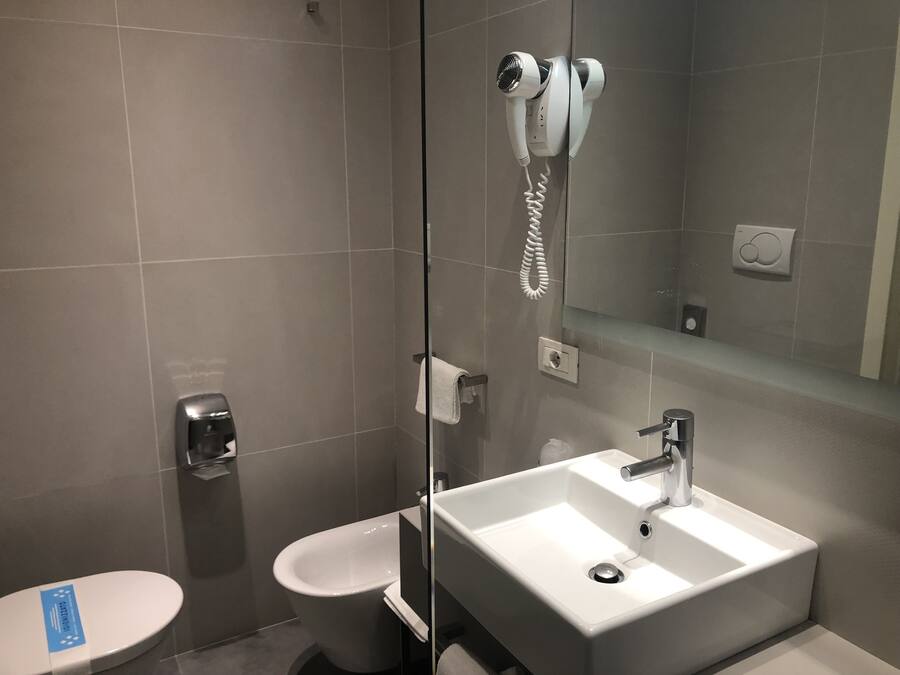 Un baño moderno con un espejo grande, un lavabo blanco y un secador de pelo de mano montado en la pared.