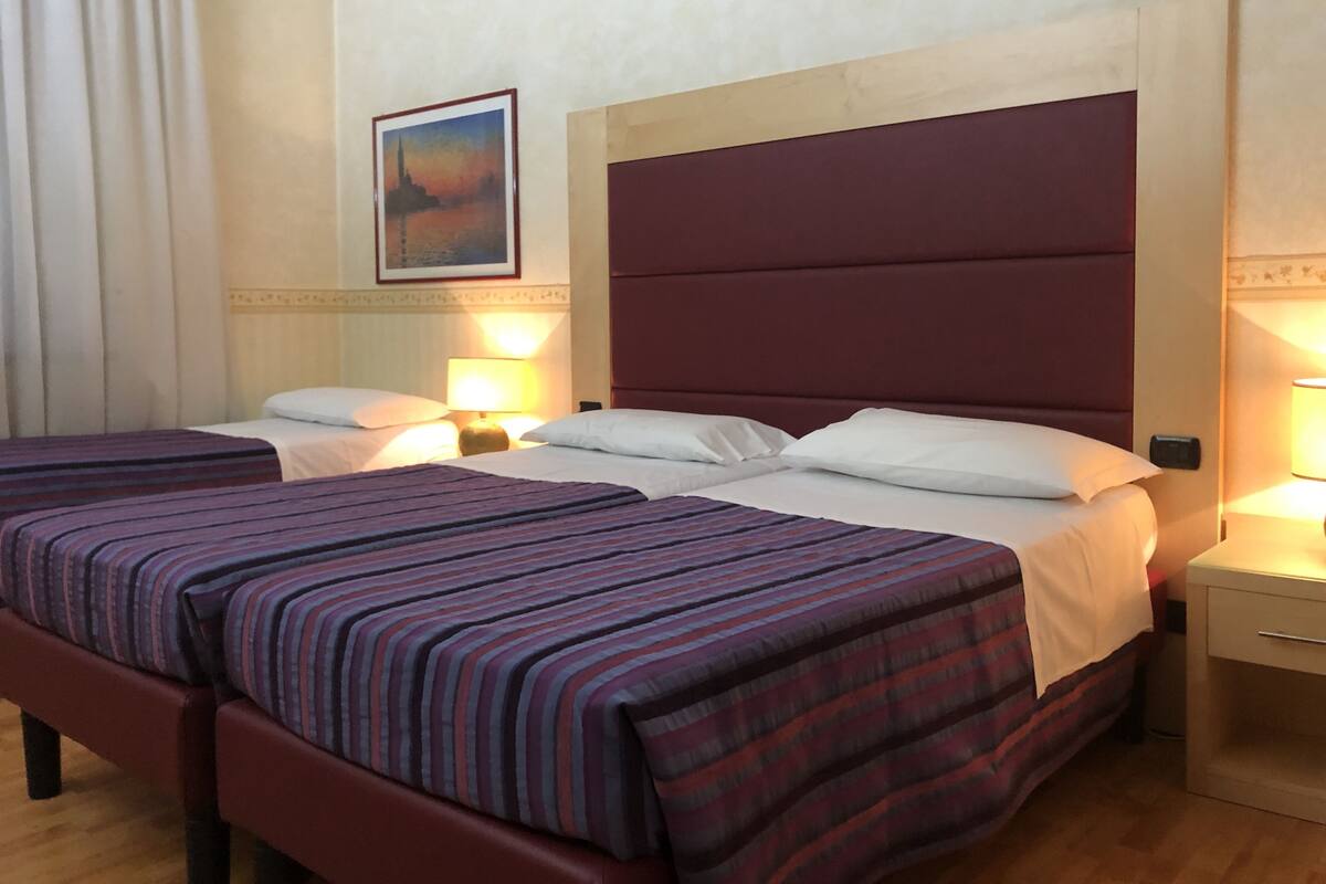 Une chambre d’hôtel avec deux lits, chacun doté de draps à rayures et d’oreillers blancs. On y trouve des tables de chevet avec des lampes, un tableau encadré au mur et un plancher en bois.
