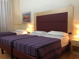Una camera d'albergo con due letti, ognuno con lenzuola a righe e cuscini bianchi. Sono presenti comodini con lampade, un quadro incorniciato appeso al muro e un pavimento in legno.