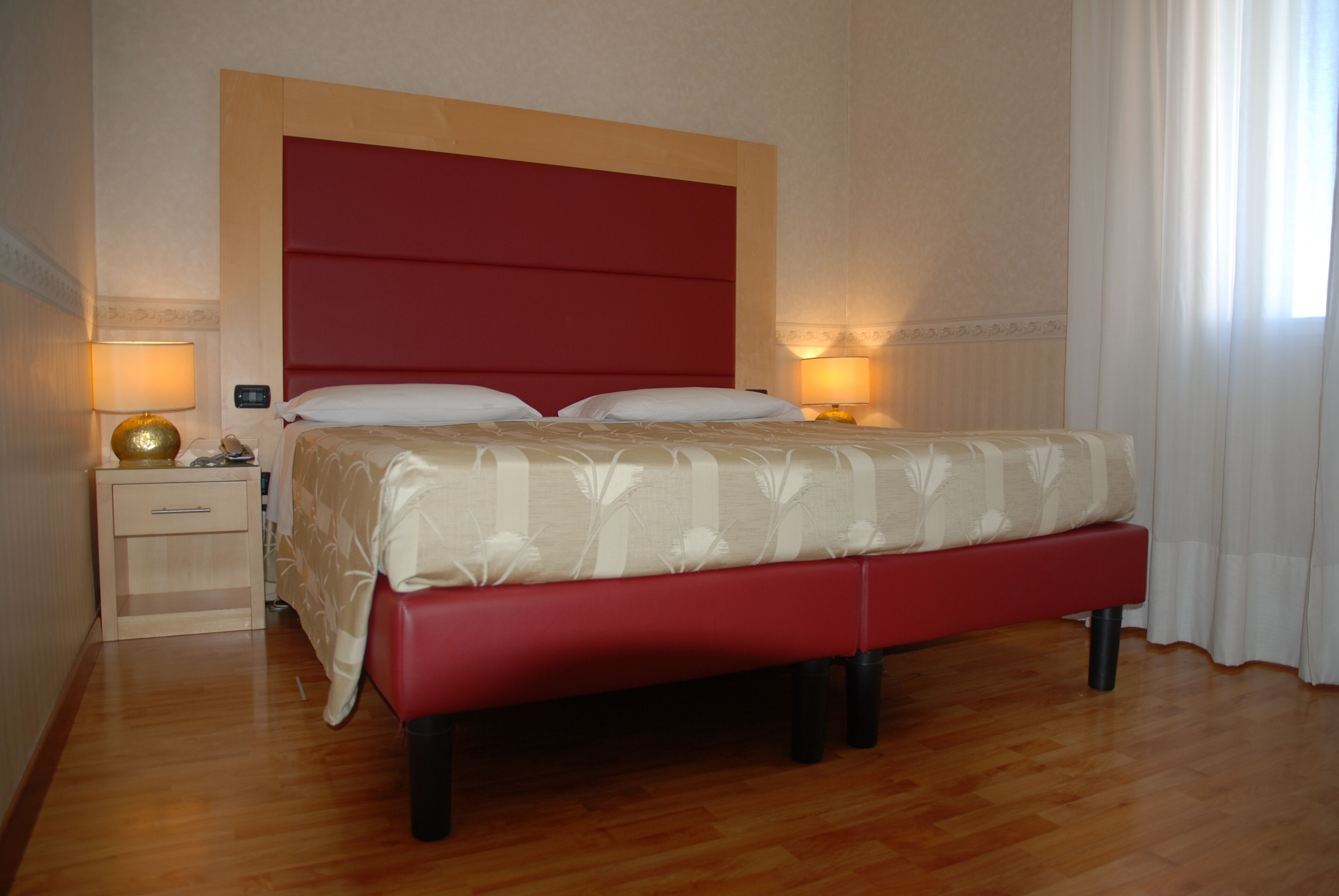 Une chambre d’hôtel avec un grand lit, un plancher en bois, une table de chevet avec une lampe et une fenêtre avec des rideaux.