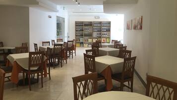 Interno di un ristorante con diversi tavoli e sedie, una vetrina per il vino e vista sulla strada.
