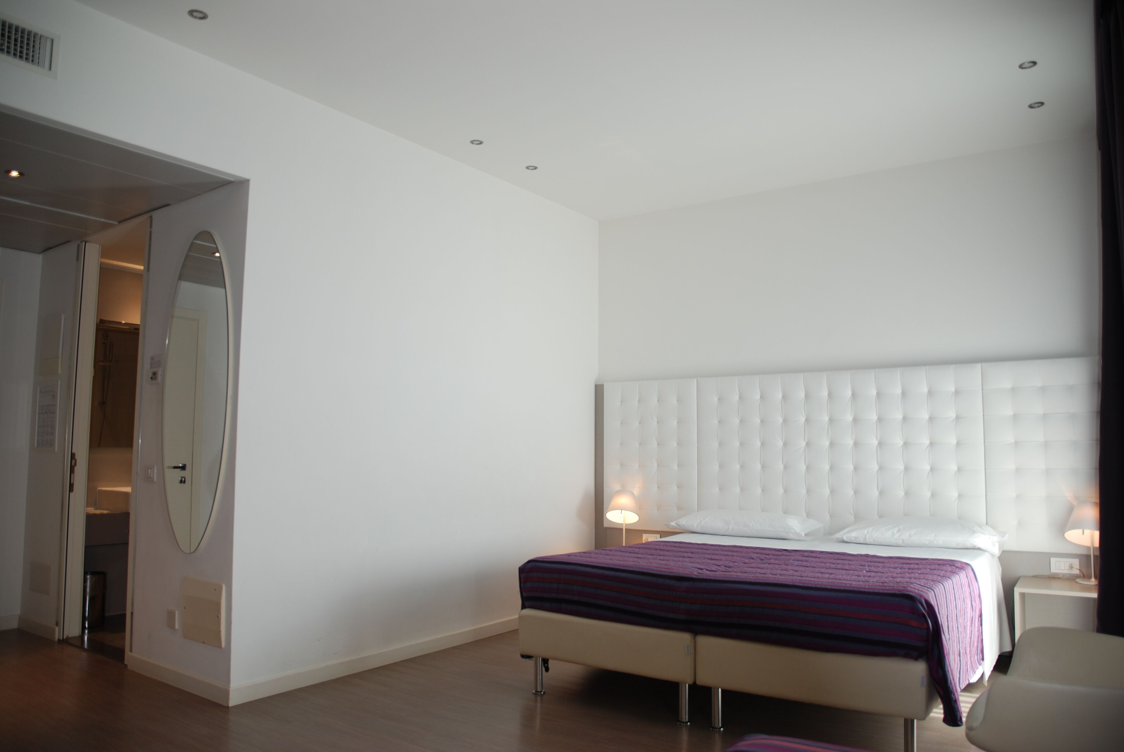 Une chambre d’hôtel moderne avec un grand lit, une table de chevet avec une lampe et un miroir au mur.