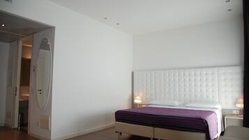 Une chambre d’hôtel moderne avec un grand lit, une table de chevet avec une lampe et un miroir au mur.