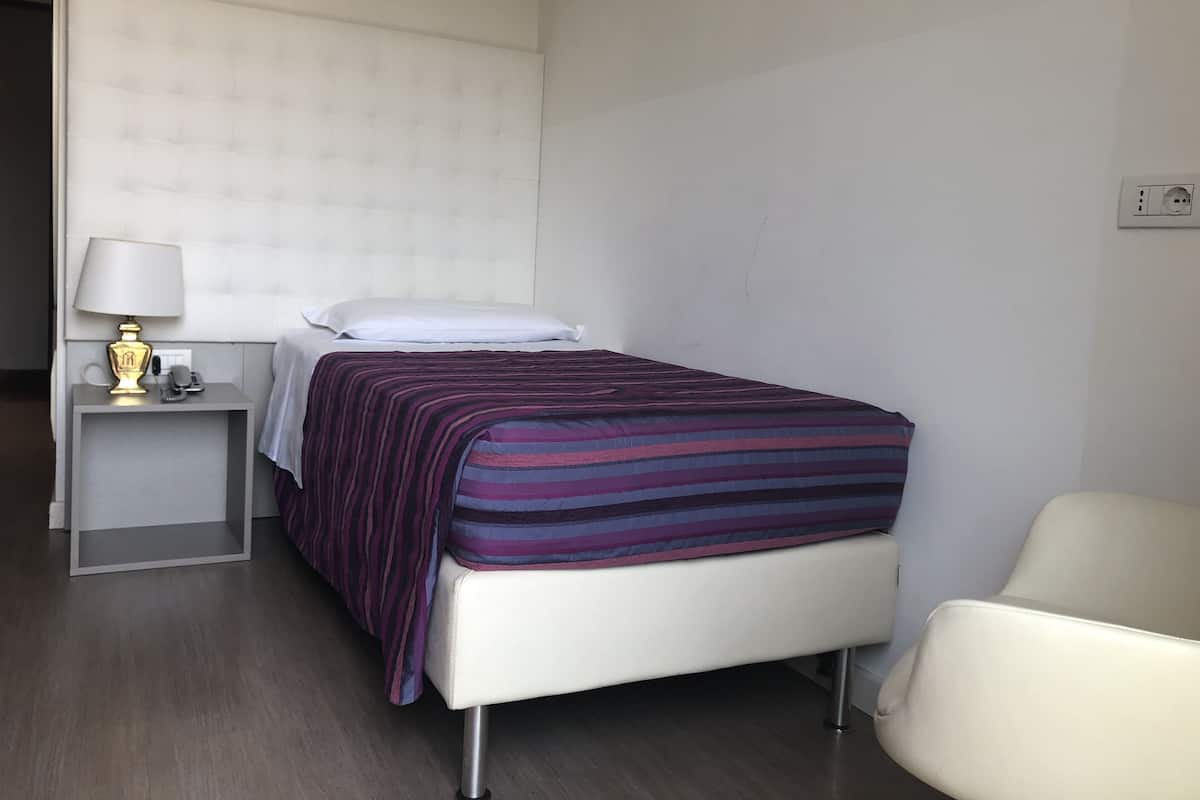Une chambre d’hôtel avec un lit, une table de chevet avec une lampe, une chaise et une prise électrique au mur.