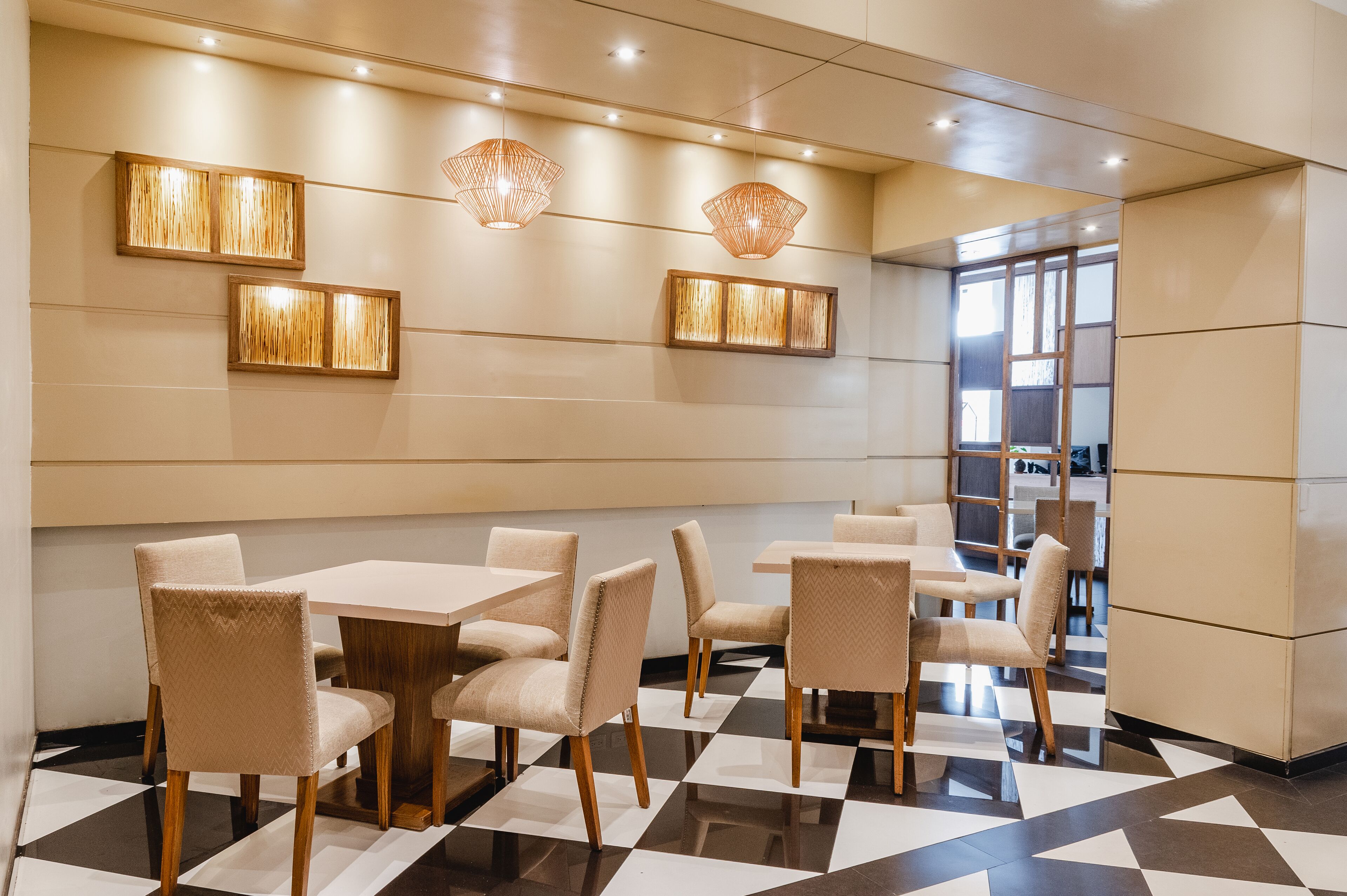 Un espace de salle à manger moderne avec un sol à carreaux, des chaises recouvertes d’un tissu beige et des luminaires suspendus.