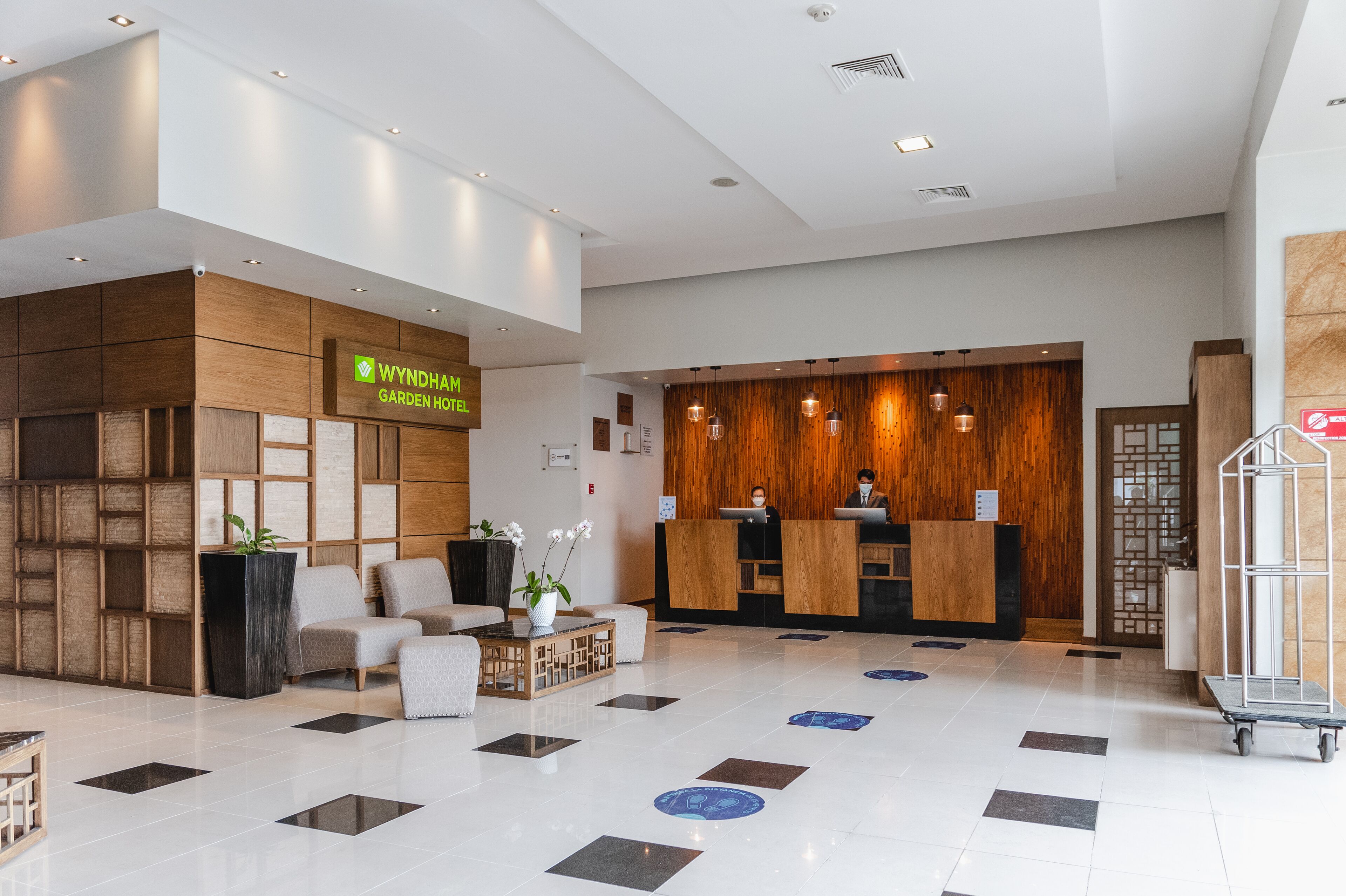 A modern hotel lobby with a reception desk, seating area, and a clean, tiled floor.