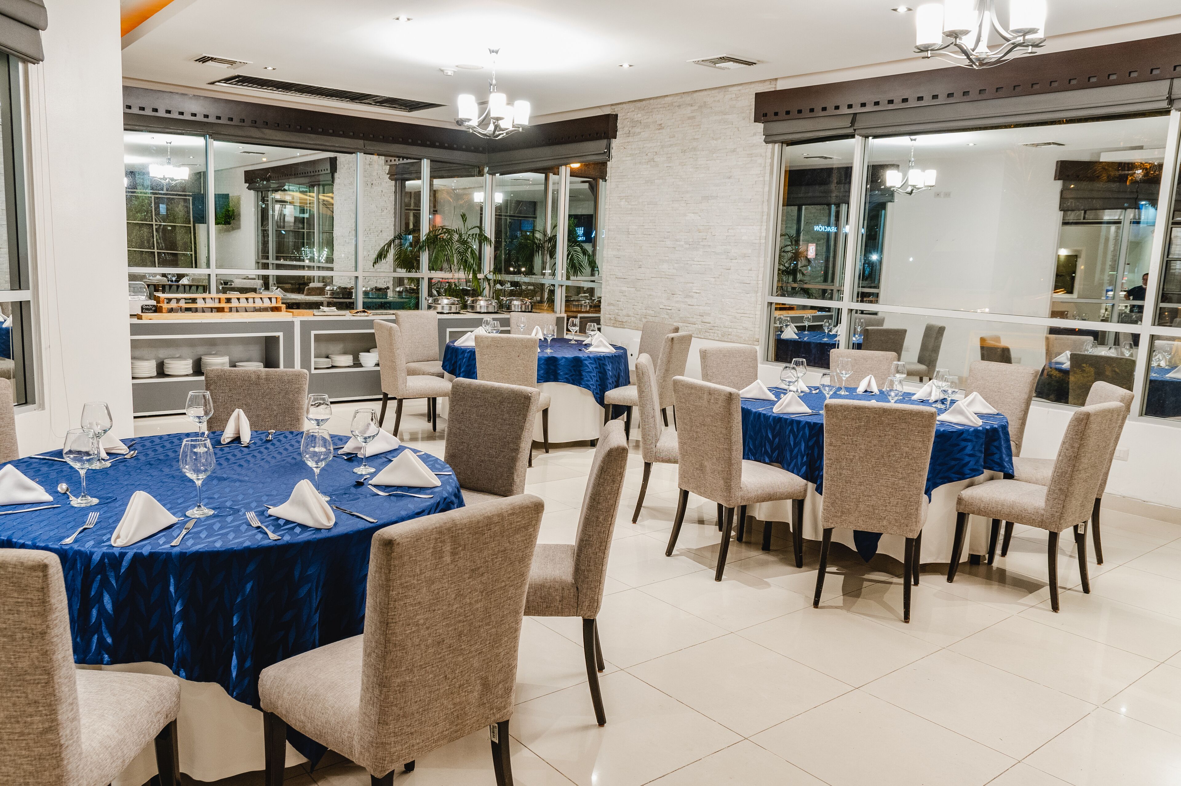 Un espace repas avec des tables rondes recouvertes de nappes bleues, des chaises beiges et des serviettes blanches.