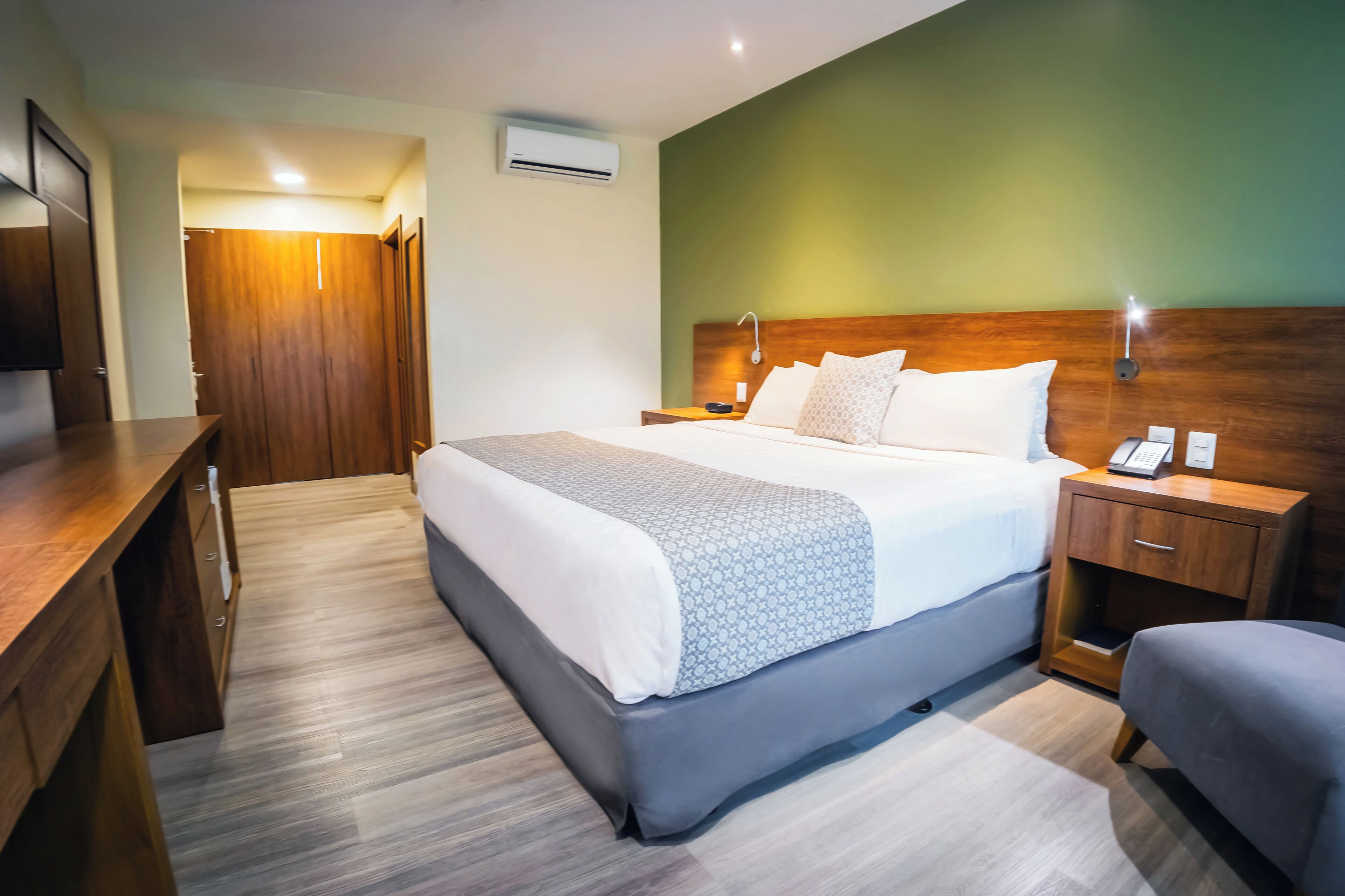 A hotel room with a large bed, bedside tables, a desk, and a wardrobe.
