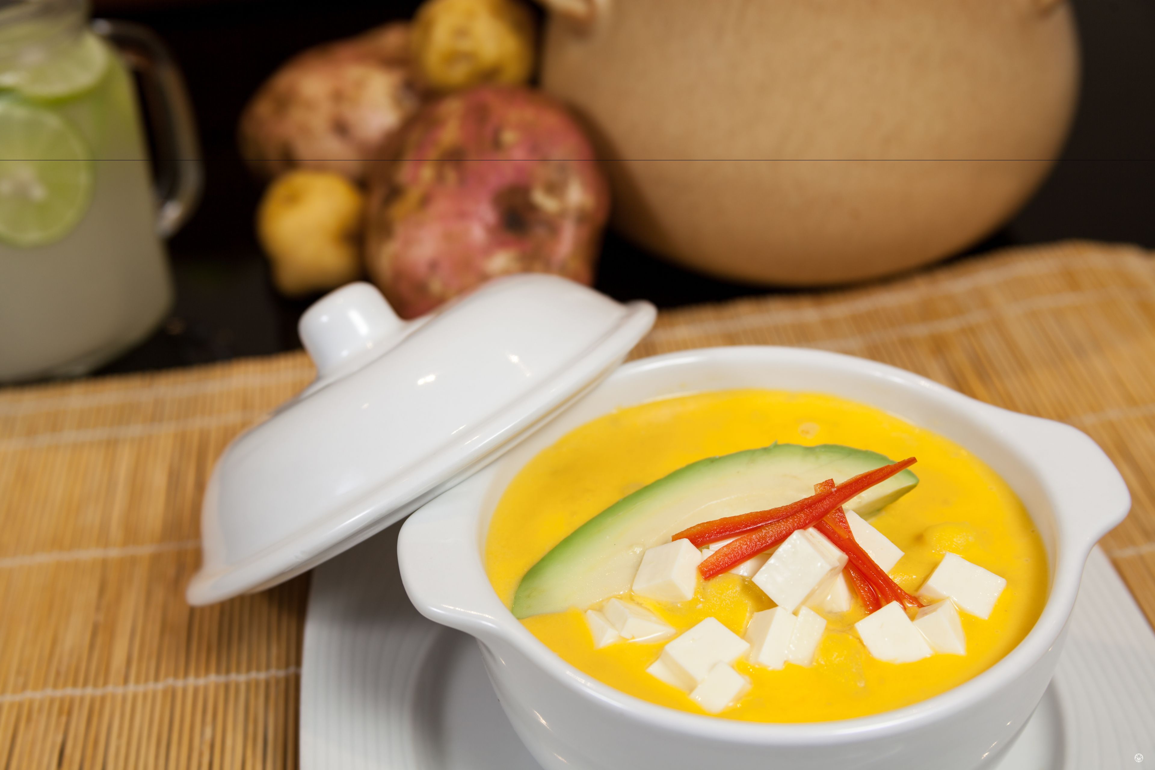 Un plato blanco con sopa, aguacate y chile rojo.