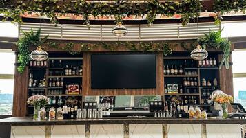 A bar area with a large flat-screen TV, shelves of liquor bottles, and wooden bar stools.