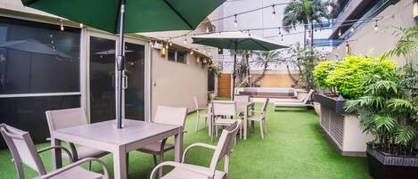 Un patio al aire libre con mesas y sillas, césped artificial verde y plantas en macetas.