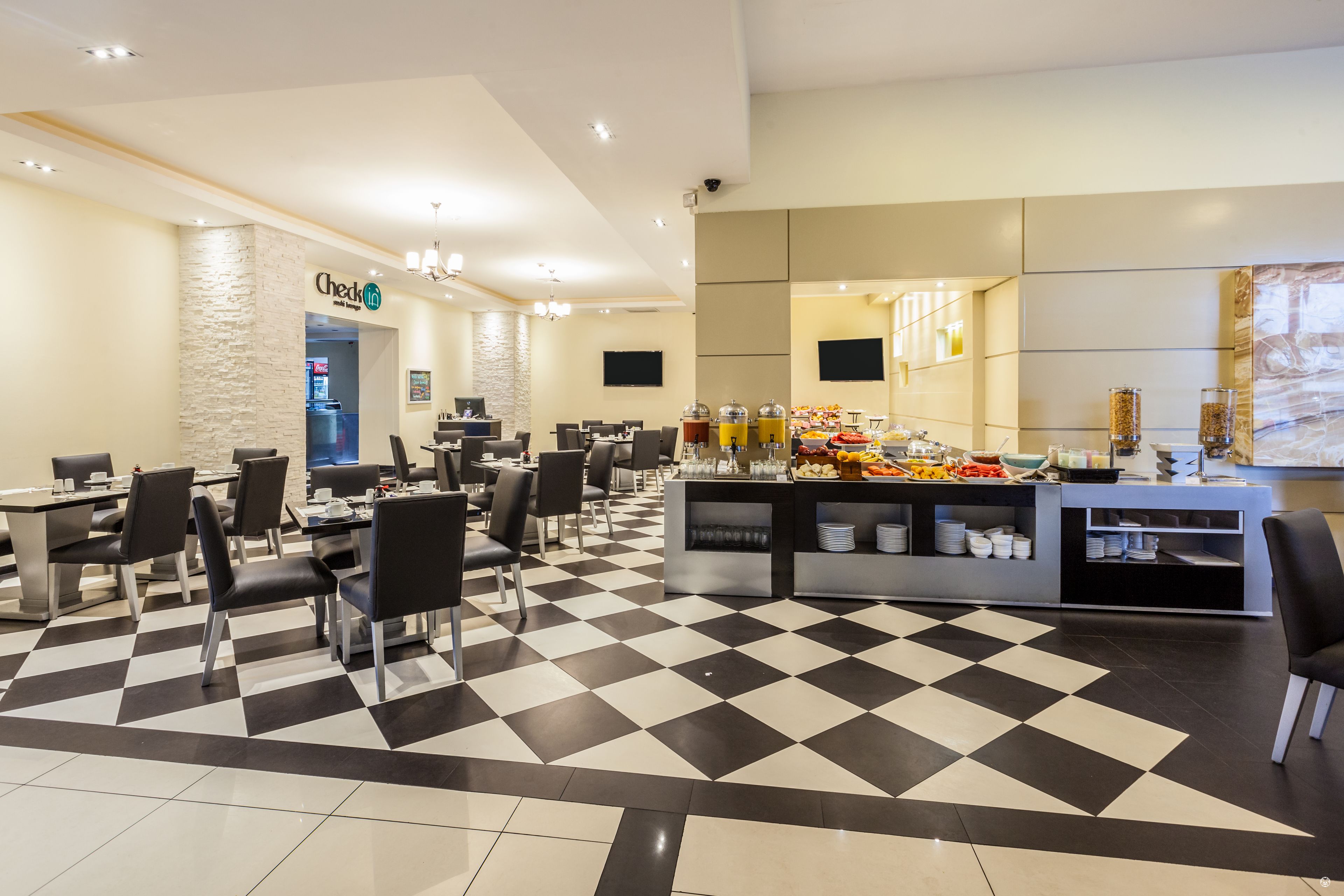 A hotel lobby with a check-in counter, a buffet area, and a seating area with tables and chairs.