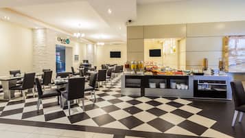 A hotel lobby with a check-in counter, a buffet area, and a seating area with tables and chairs.
