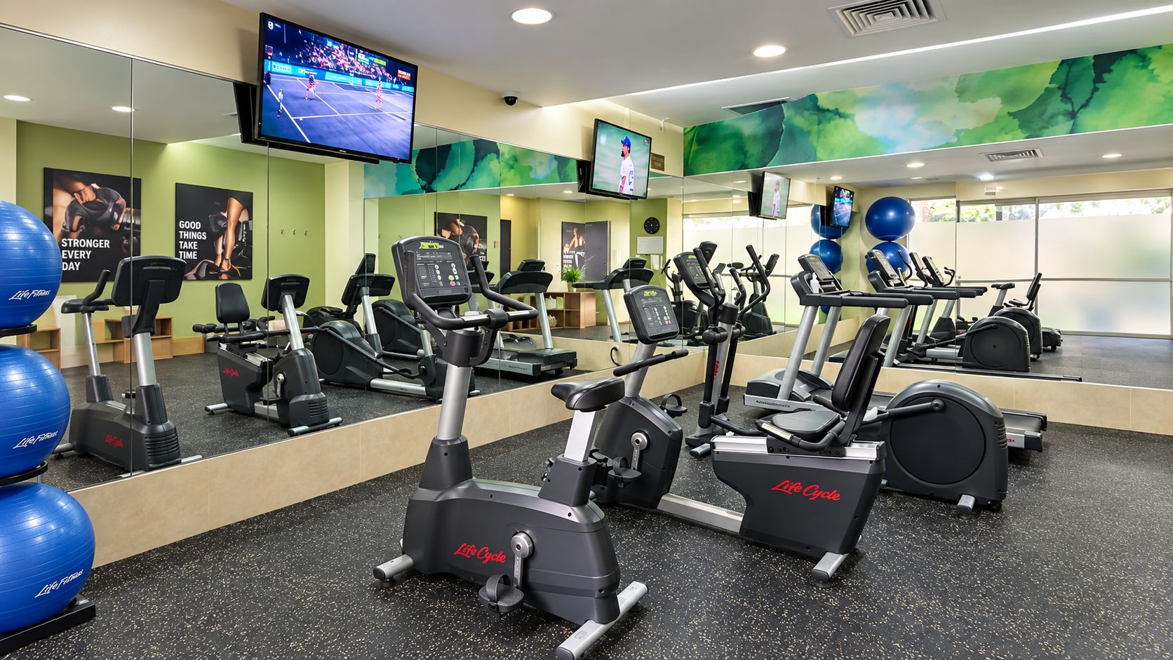 Une salle de sport équipée de nombreux appareils de cardio, de ballons d’exercice et d’un grand miroir.