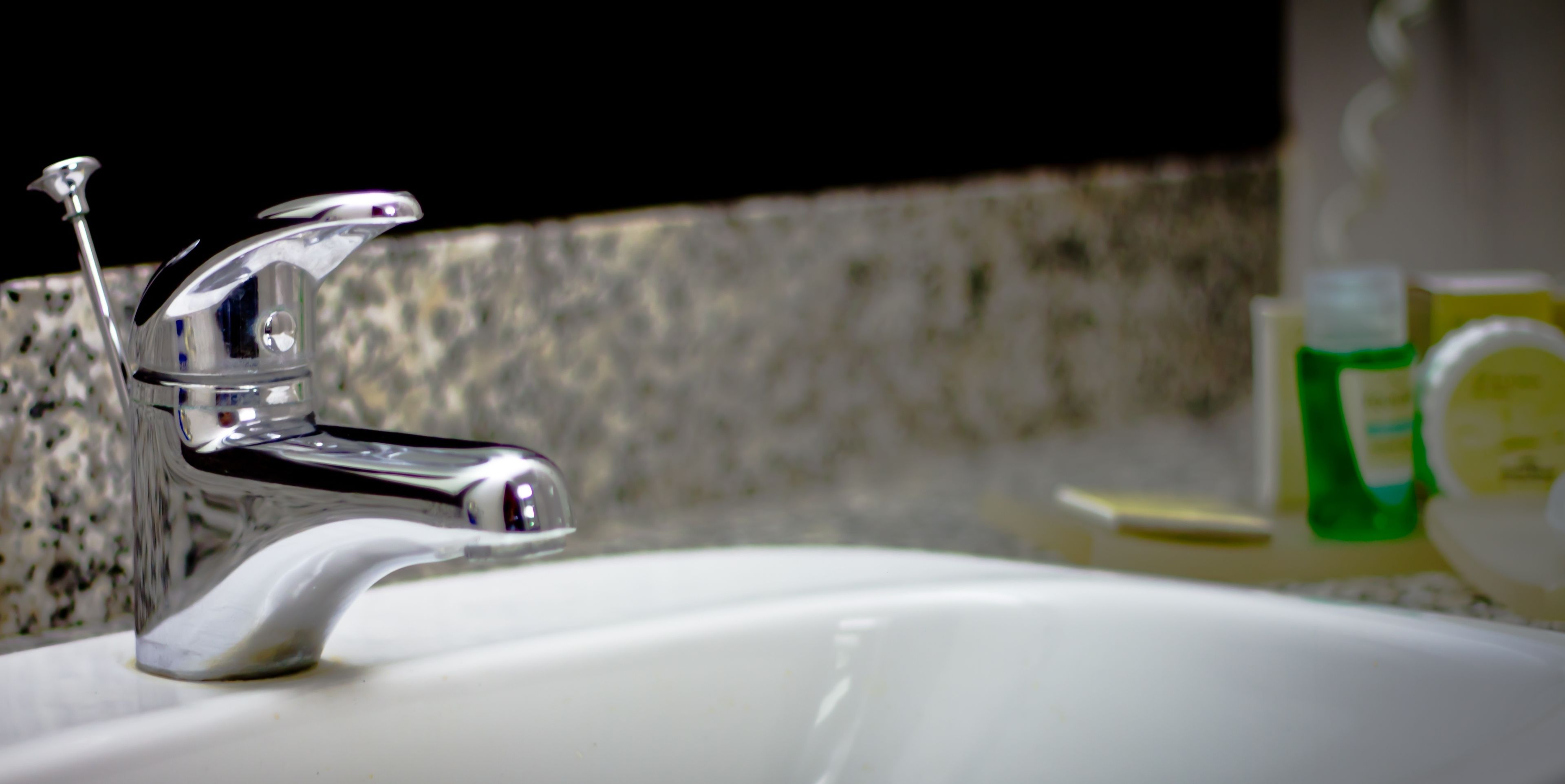 A bathroom sink with a chrome faucet and a soap dispenser in the background.