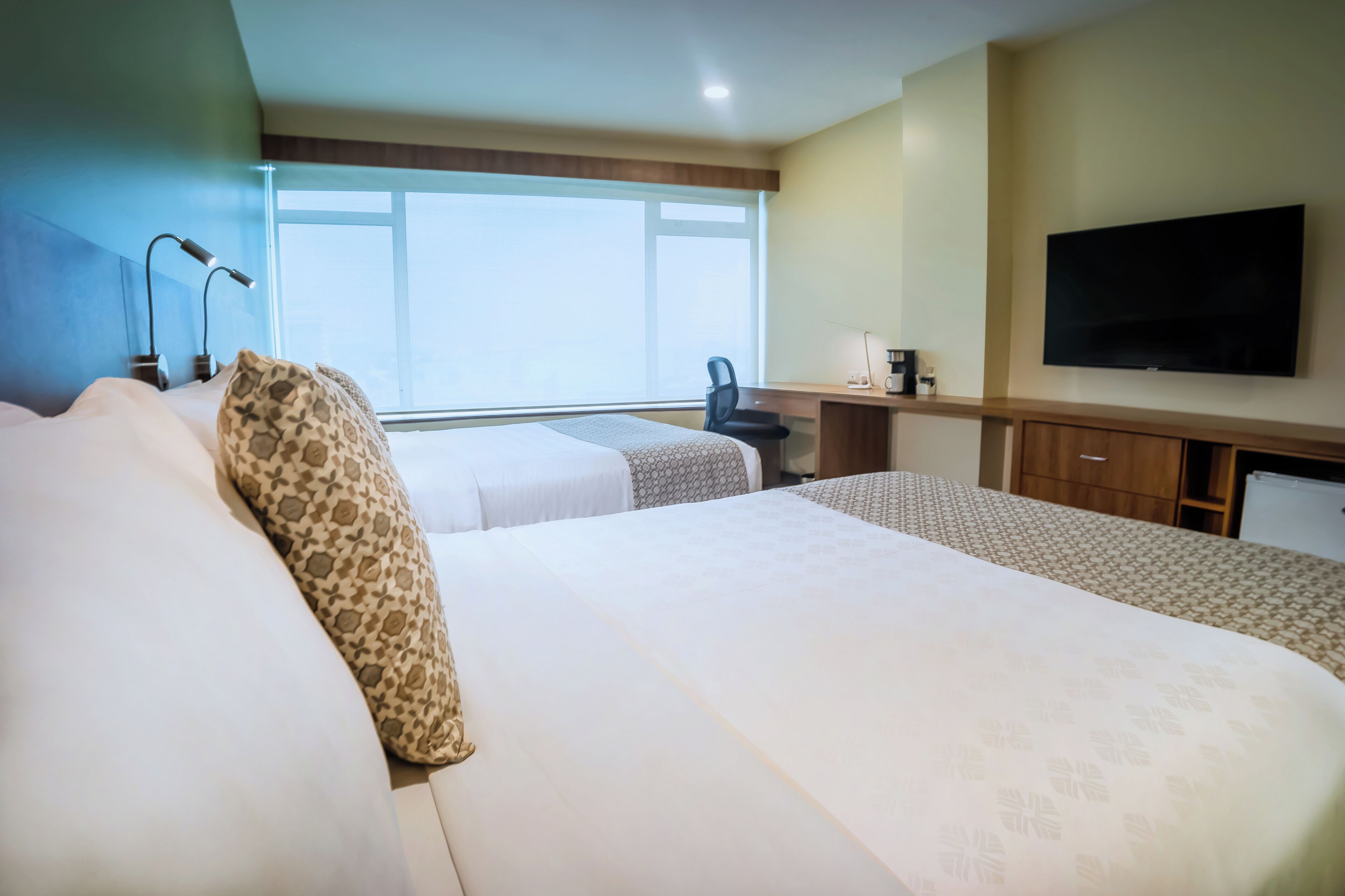 Habitación de hotel con dos camas, un escritorio, una silla, un televisor y un ventanal grande.