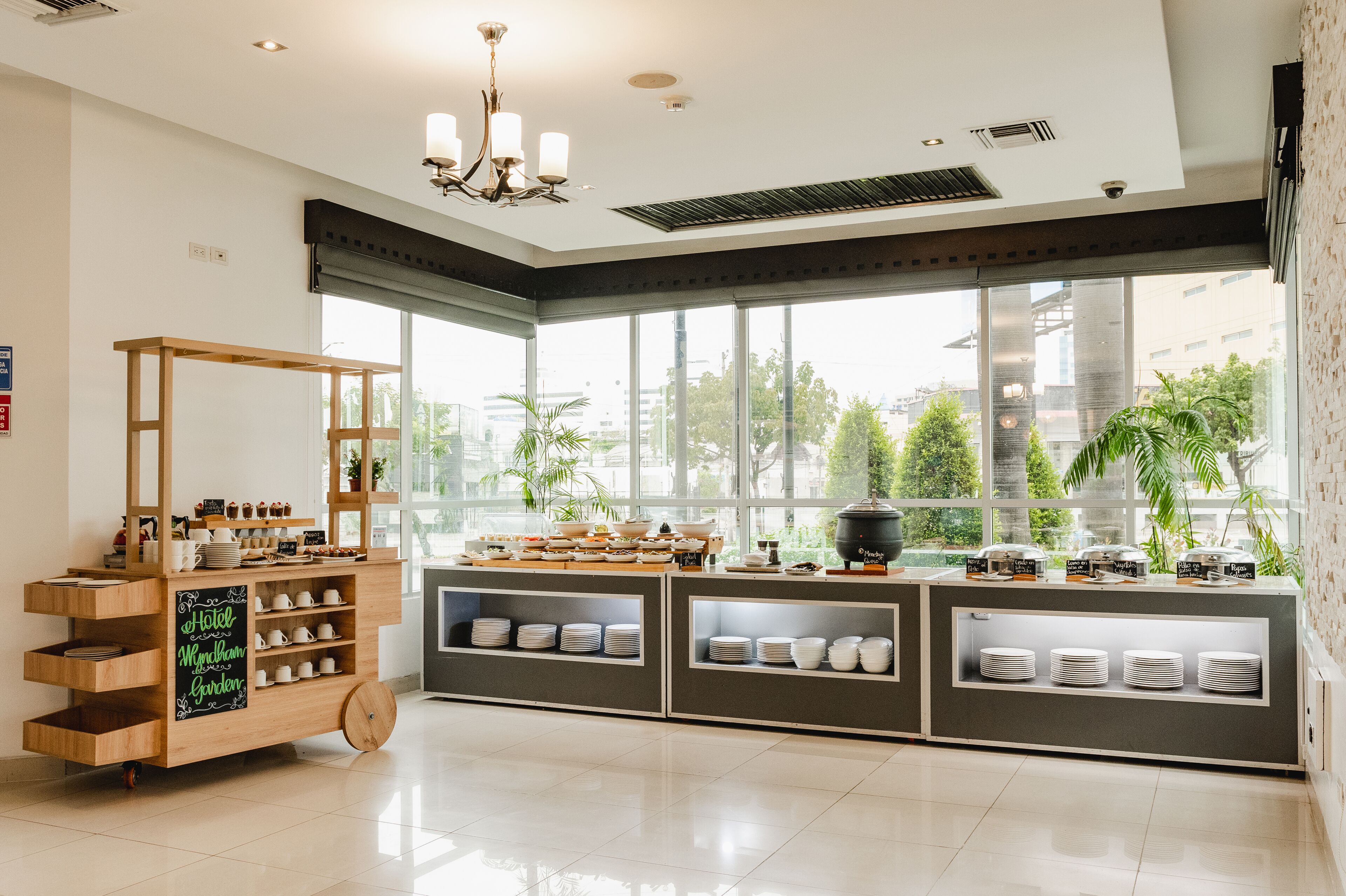 Una habitación de hotel con un ventanal grande, un carrito de madera con vajilla y una zona de kitchenette.