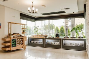 Una habitación de hotel con un ventanal grande, un carrito de madera con vajilla y una zona de kitchenette.