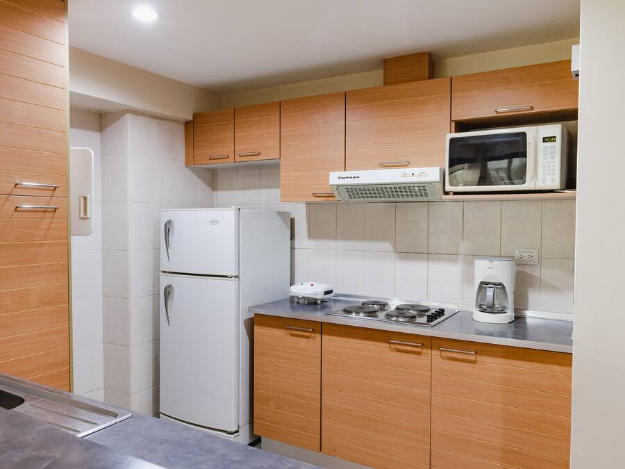 Una cocina moderna con armarios de madera, un refrigerador blanco, un microondas y una cafetera en la encimera.