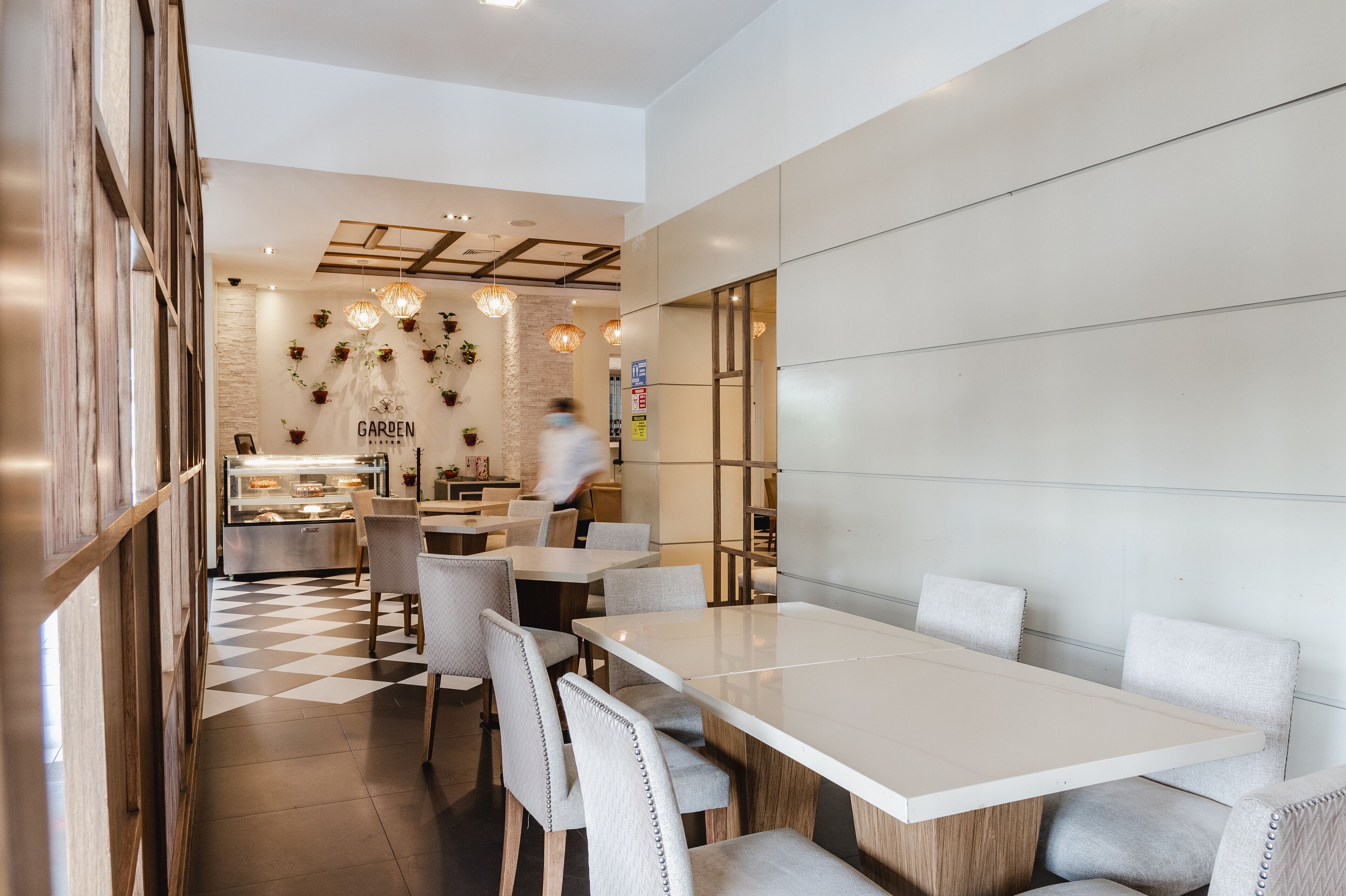 Un interior de restaurante moderno con suelo a cuadros, mesas blancas y sillas grises.