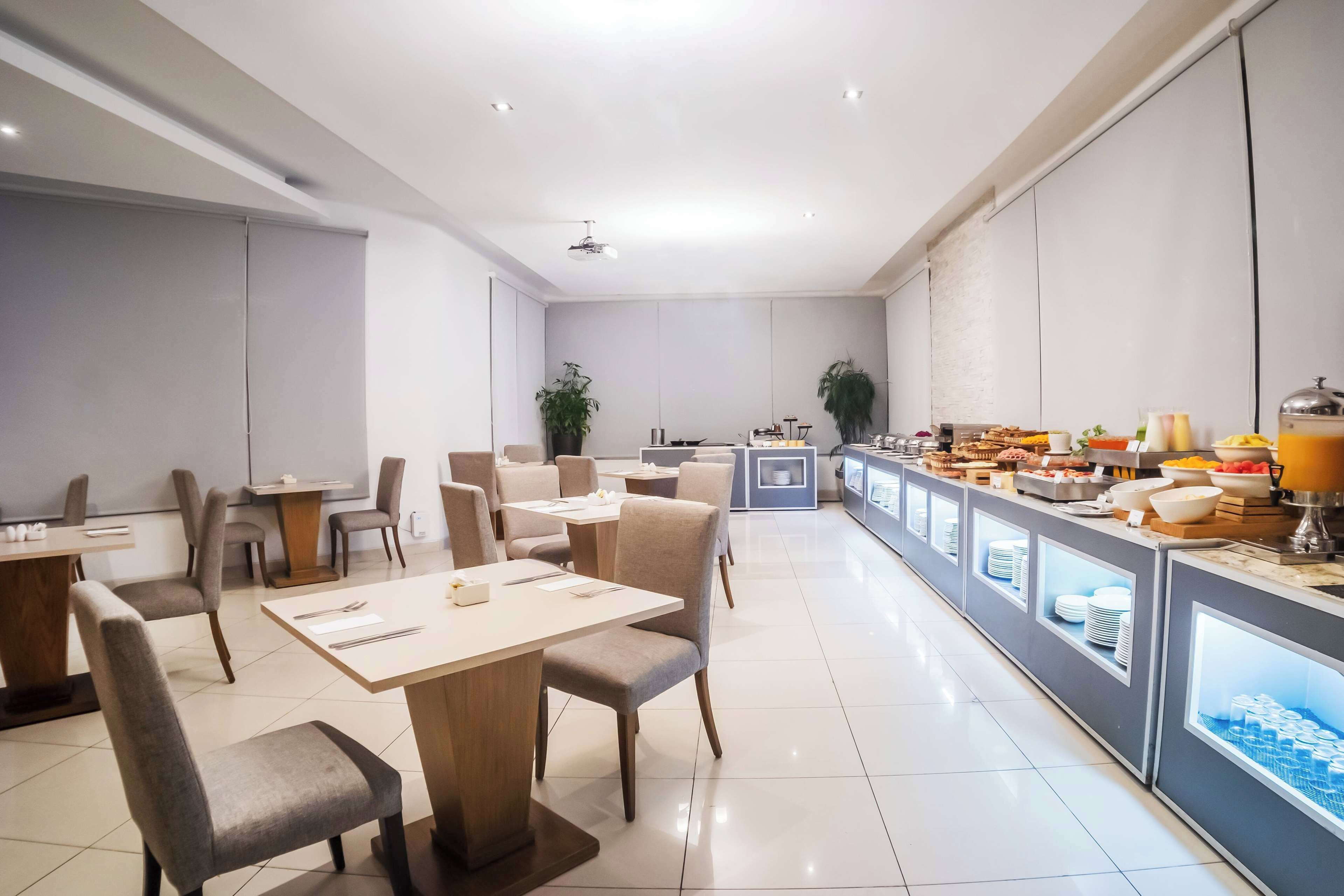 A modern dining area with tables and chairs, a buffet counter with various food items, and a clean, minimalist design.