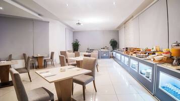 A modern dining area with tables and chairs, a buffet counter with various food items, and a clean, minimalist design.