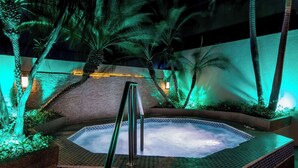 Un jacuzzi rodeado de palmeras y un muro de ladrillo, con una barandilla metálica en primer plano.