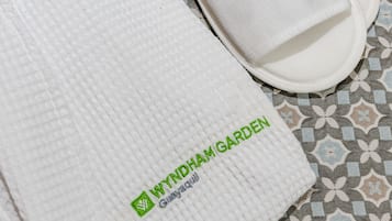 A pair of white slippers with green text on the sole and a white textured mat with green text.