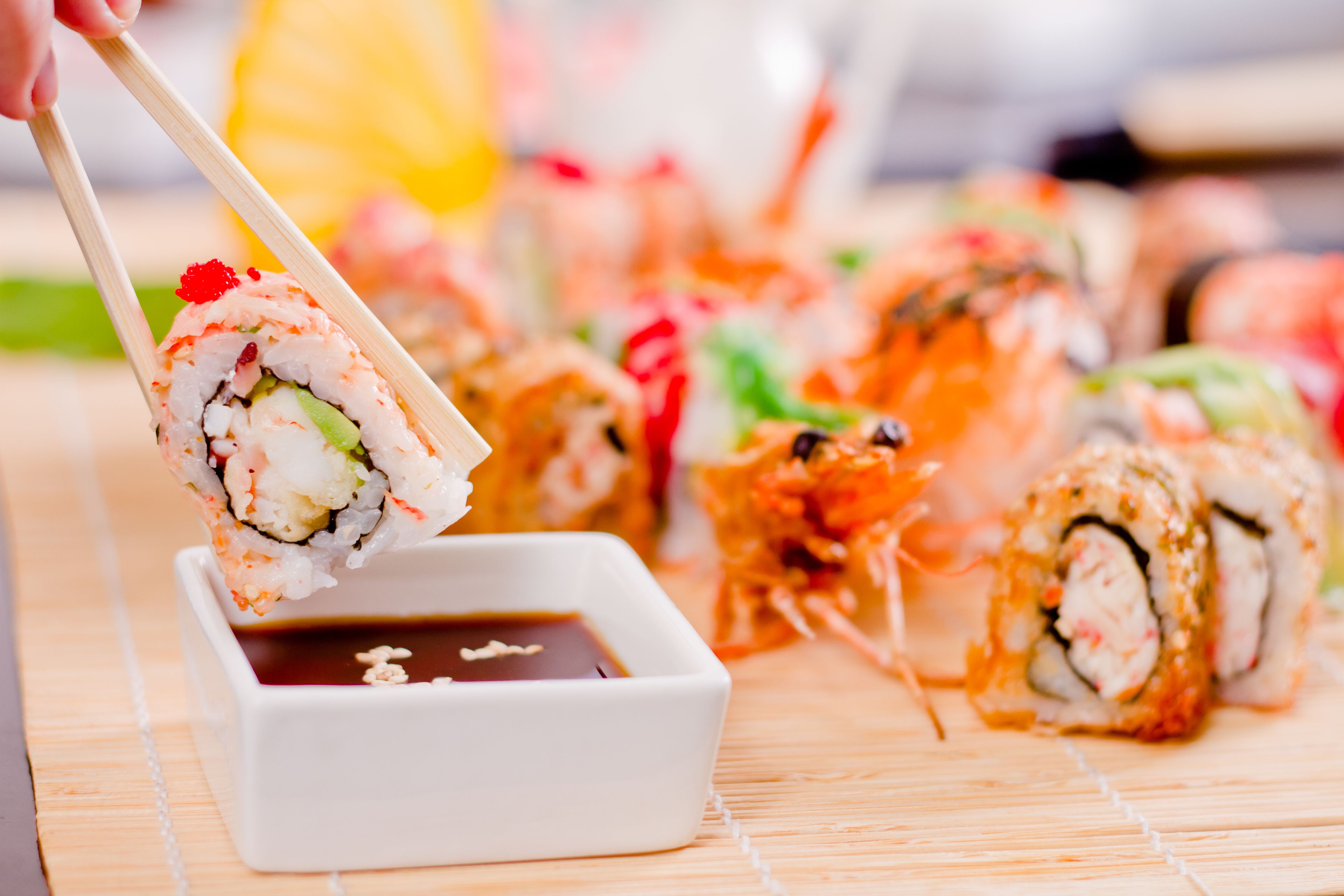 Variedad de rollos de sushi sobre una estera de bambú, con un recipiente pequeño de salsa de soja.