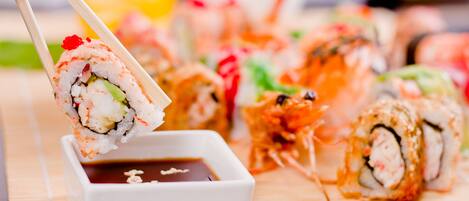 Variedad de rollos de sushi sobre una estera de bambú, con un recipiente pequeño de salsa de soja.