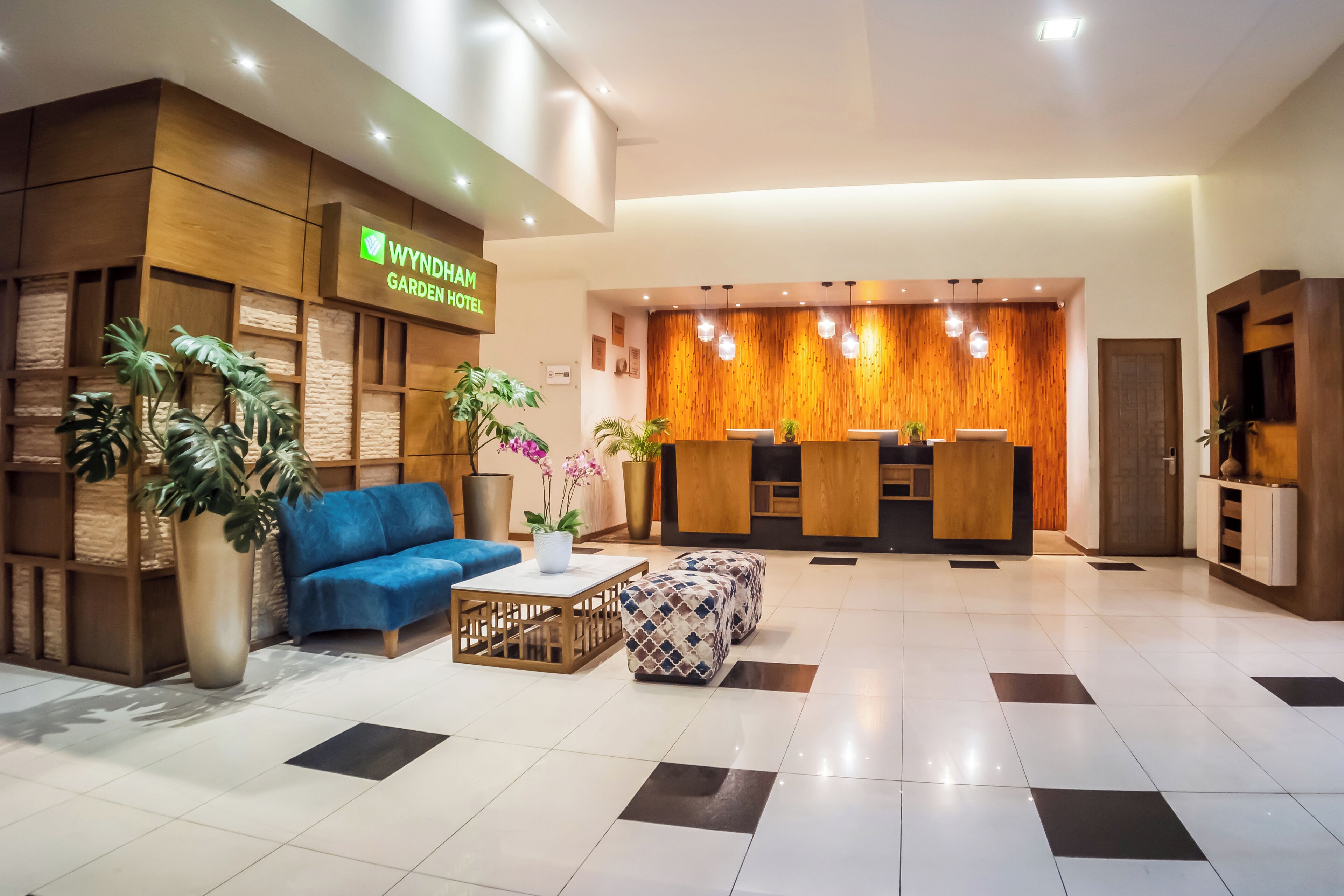 A hotel reception area with a wooden reception desk, a blue sofa, and potted plants.