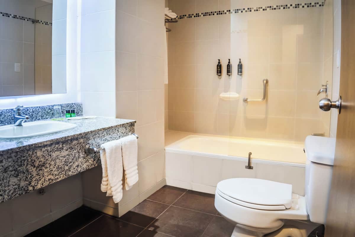 A modern bathroom with a marble countertop, a white toilet, a bathtub, and a shower area.