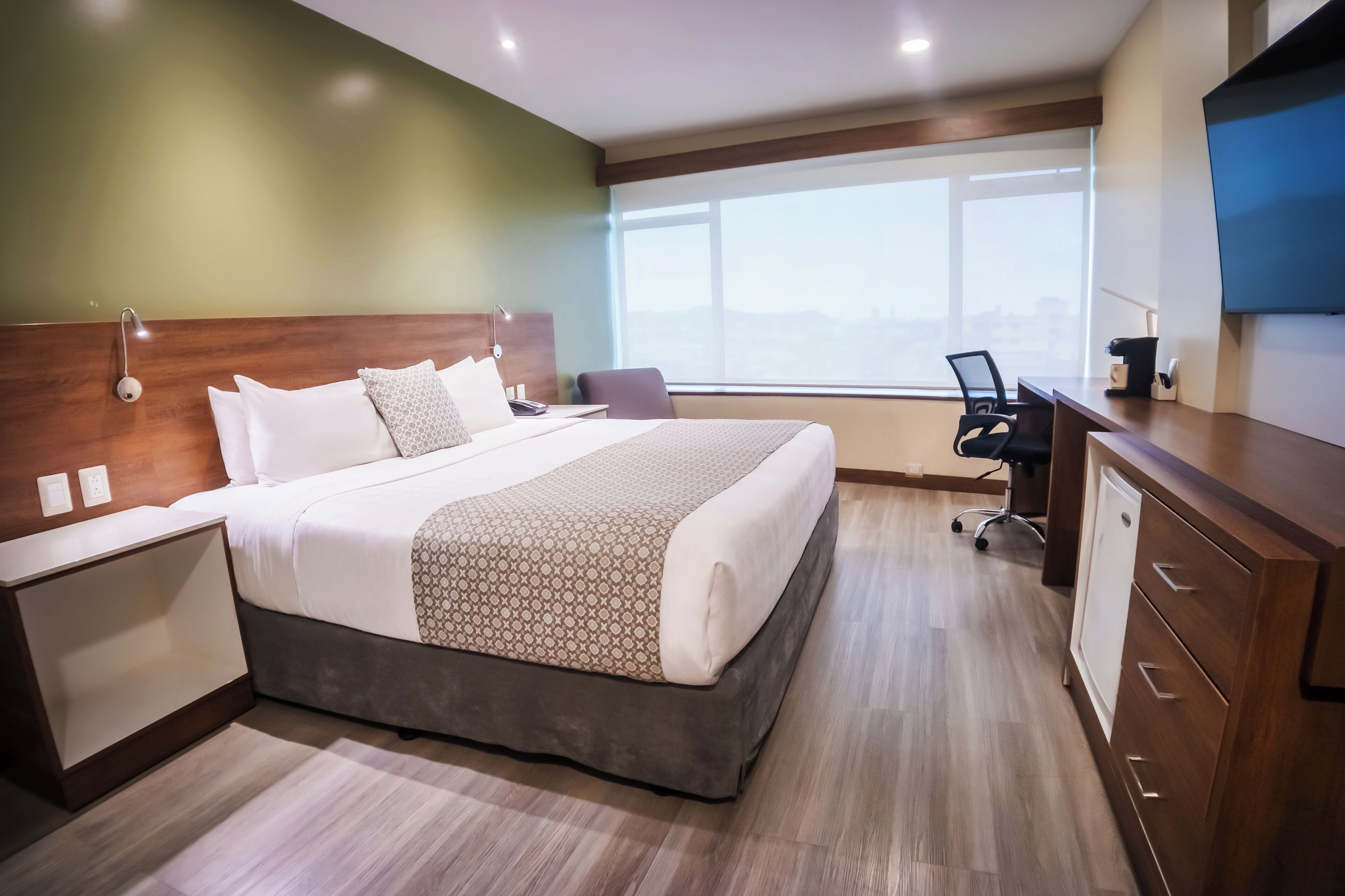 A hotel room with a large bed, a desk, a chair, and a TV.
