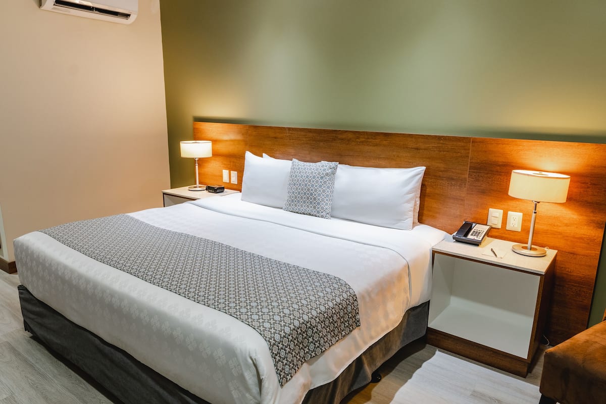 A hotel room with a large bed, two bedside tables, a wooden headboard, and two bedside lamps.
