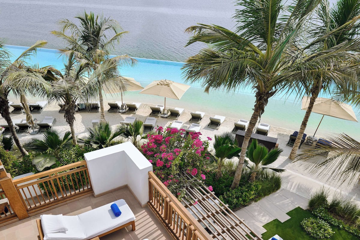 A resort balcony with lounge chairs, a pool, and a view of the beach.