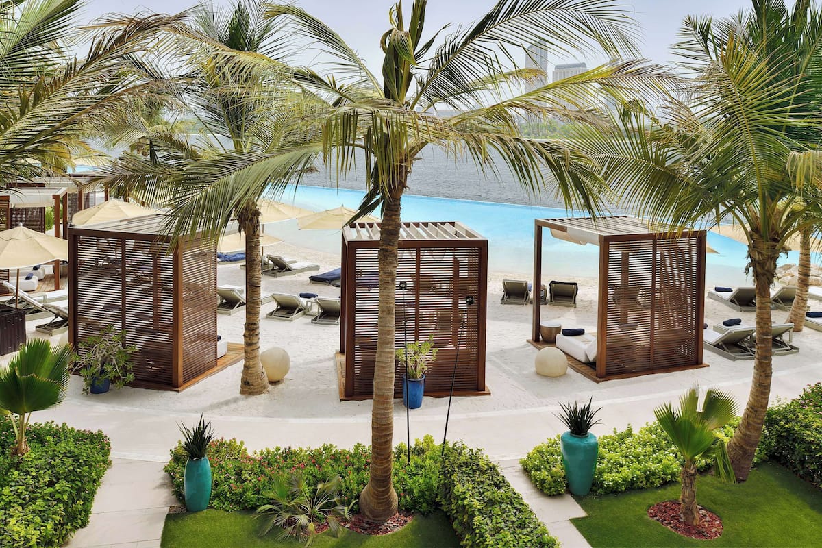 A beachside resort with palm trees, lounge chairs, and umbrellas.