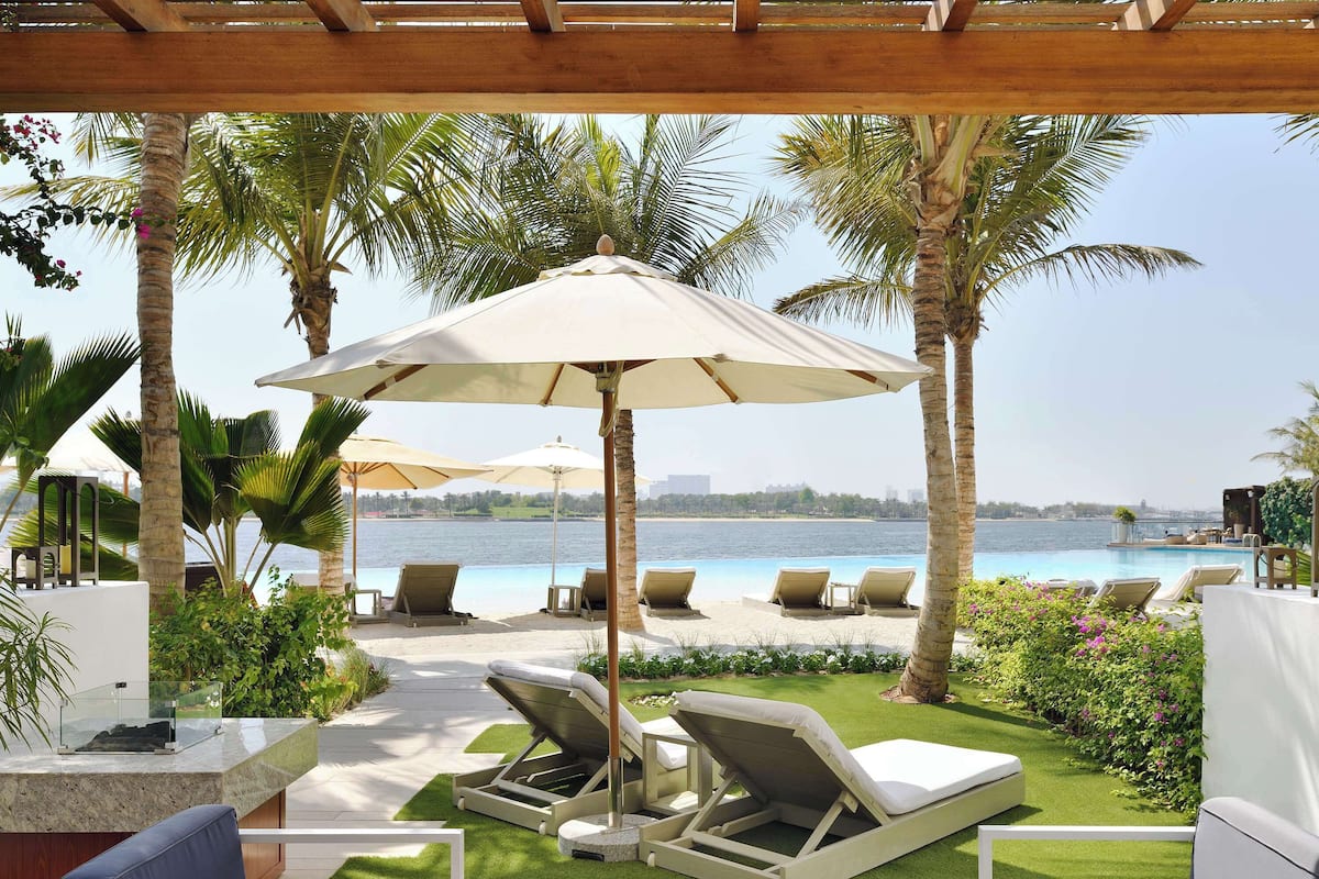 A poolside area with lounge chairs and umbrellas, surrounded by palm trees and a view of the water.