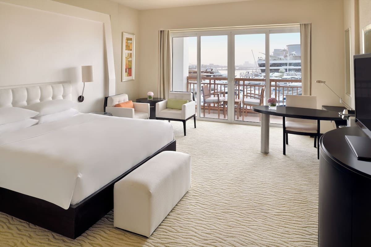 A hotel room with a large bed, a desk, a chair, a TV, and a balcony with a view of the city.