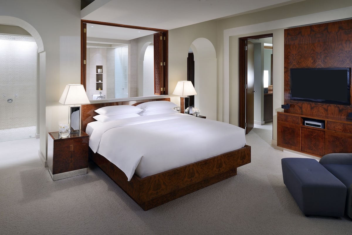 A modern hotel room with a large bed, bedside lamps, a TV, and a wooden cabinet.