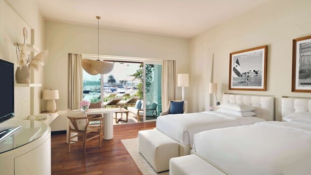 Camera d'albergo con un ampio letto, una scrivania con sedia, televisione e vista sulla spiaggia.