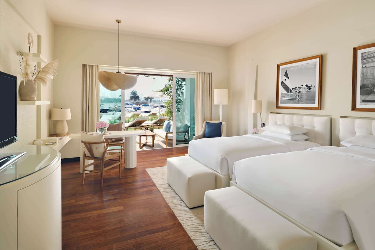 A hotel room with a large bed, a desk with a chair, a TV, and a view of the beach.