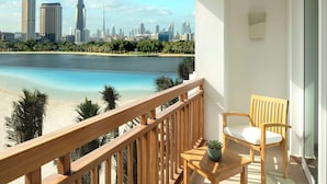 A balcony with a wooden railing, a wooden chair, a small table, and a potted plant. A city skyline and beach are visible in the background. - Park Hyatt Dubai (Dubai)