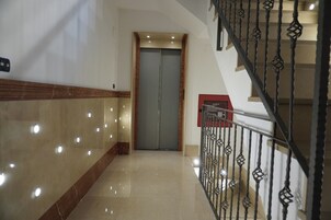 Un couloir doté d’un sol en marbre, d’un mur d’accent en bois, d’une porte fermée et d’un escalier avec une rampe en métal.