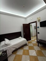 Habitación de hotel con cama, mesita de noche, teléfono, televisor montado en la pared y quiosco de registro.