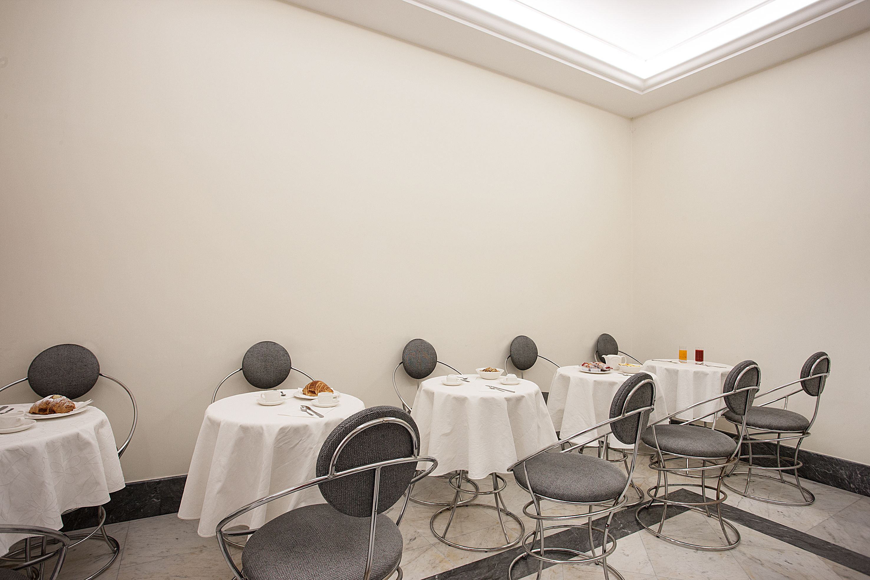 A conference room with round tables and chairs, white tablecloths, and a marble floor.