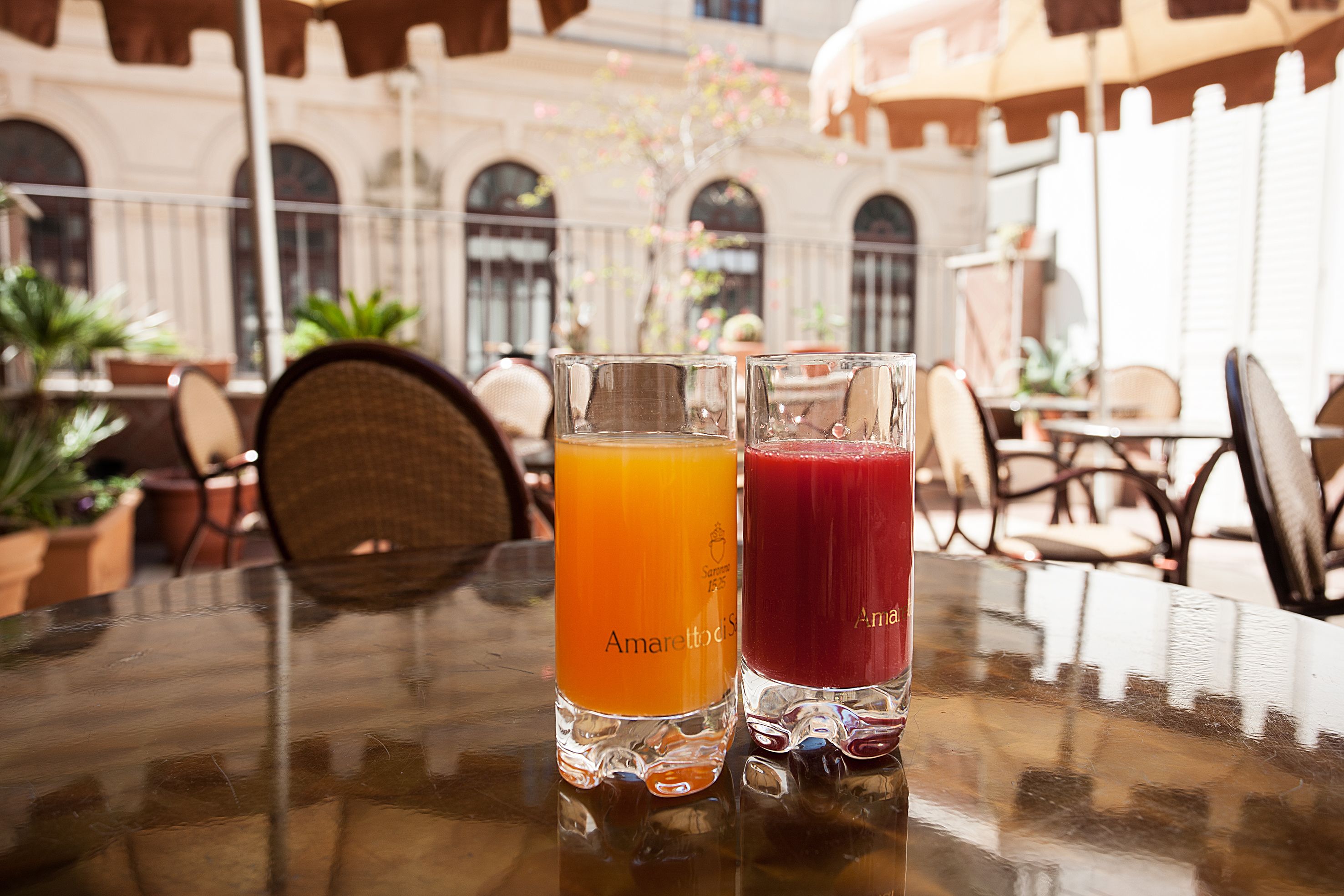 Two glasses of juice on a table in an outdoor cafe setting with a classic architectural background.