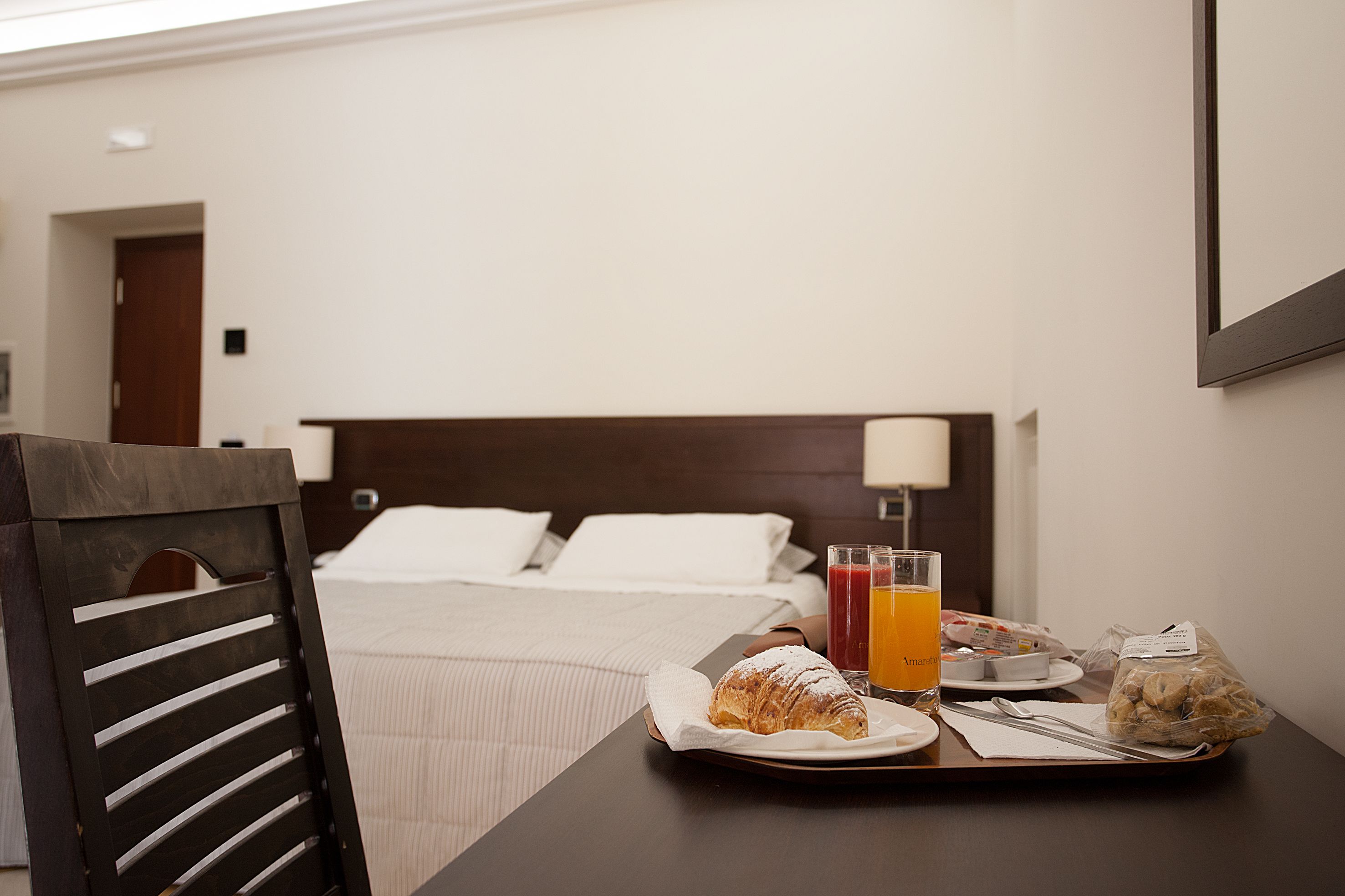 Una camera d'albergo con un vassoio per la colazione ordinato su un tavolo, con croissant, succo d'arancia e cereali.