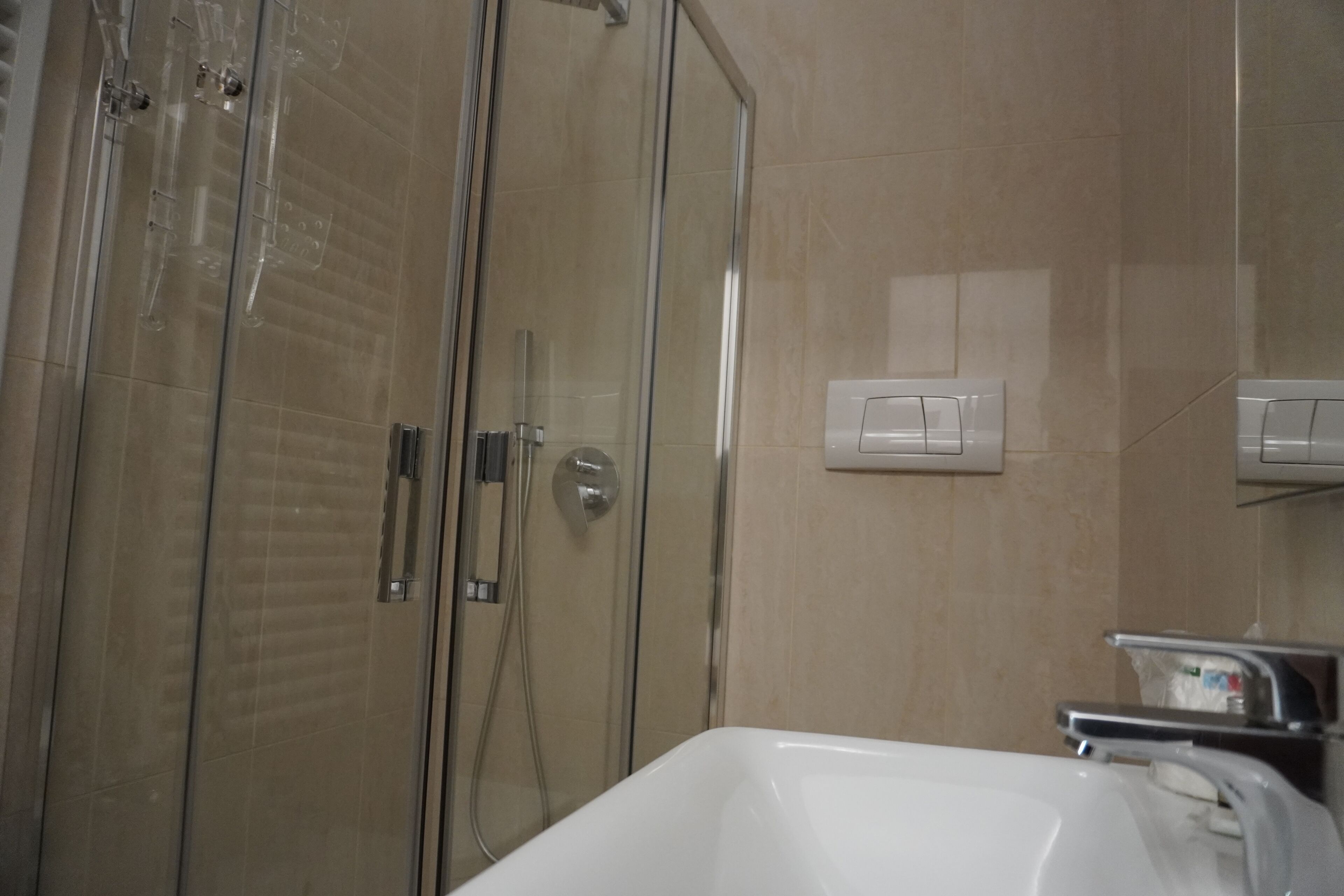 A bathroom with a glass shower enclosure, a white sink, and a wall-mounted light switch.