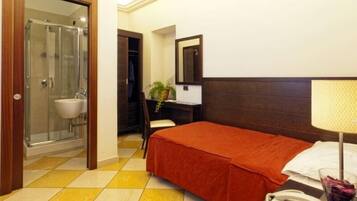 Una camera d'albergo con un letto, un comodino con una lampada, un telefono e un bagno con doccia e lavandino.