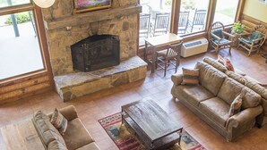 A spacious living room with a stone fireplace, large windows, and comfortable seating. - Lake Chatuge Lodge (Hiawassee)